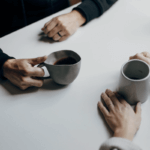 close up of hands holding coffee mugs on table
