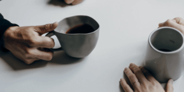 close up of hands holding coffee mugs on table