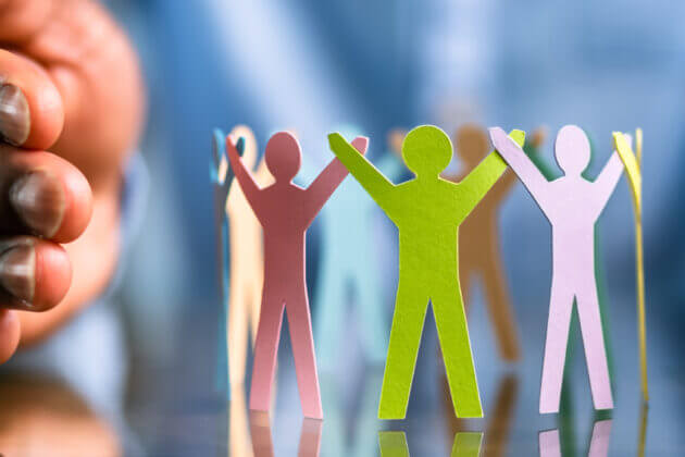 close up of hands protecting paper shapes of figures representing safeguarding