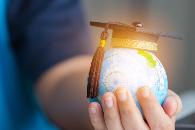 hand holding globe with mortarboard perched on top