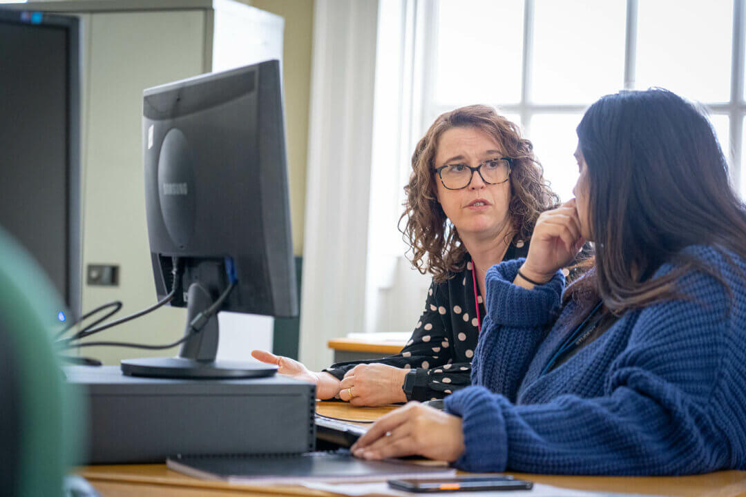 two women sitting at a desk with a computer