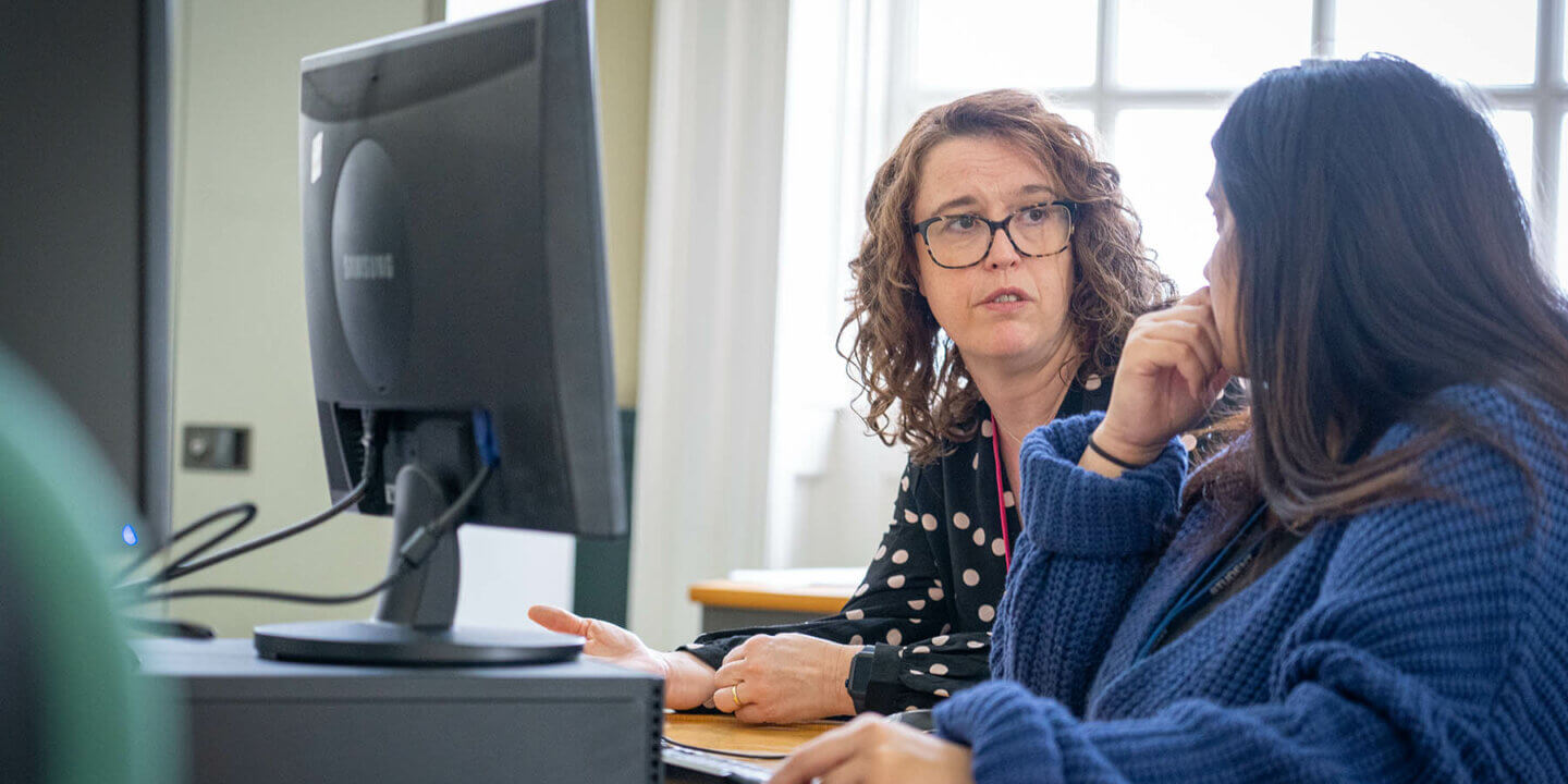 two women sitting at a desk with a computer