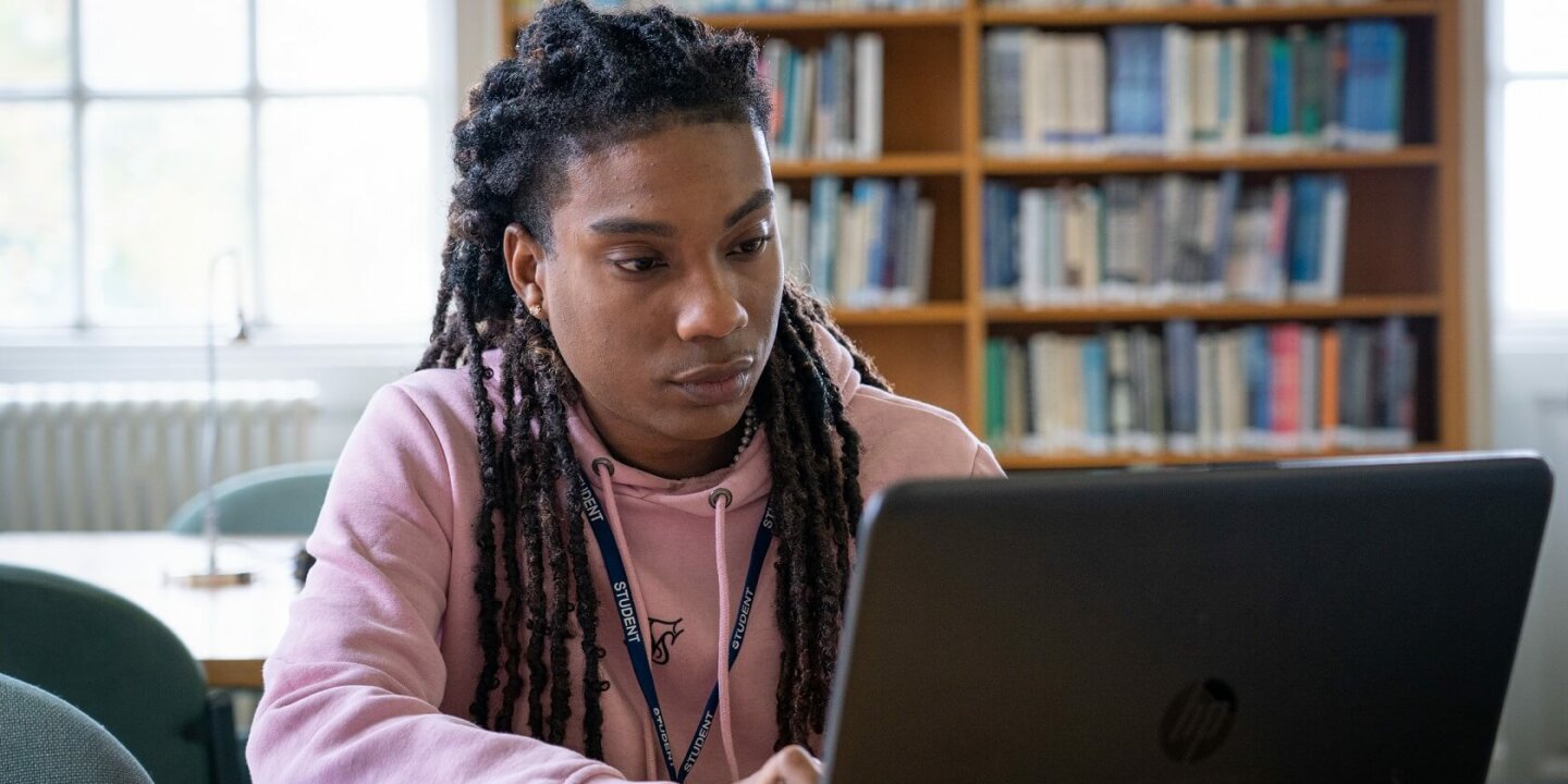 student working on a laptop with shelves of books in the background