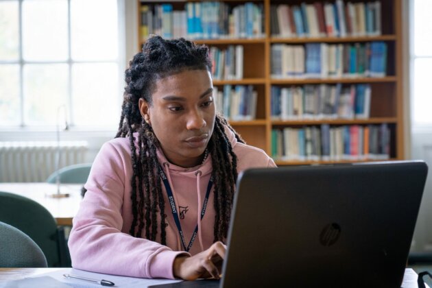 student working on a laptop with shelves of books in the background